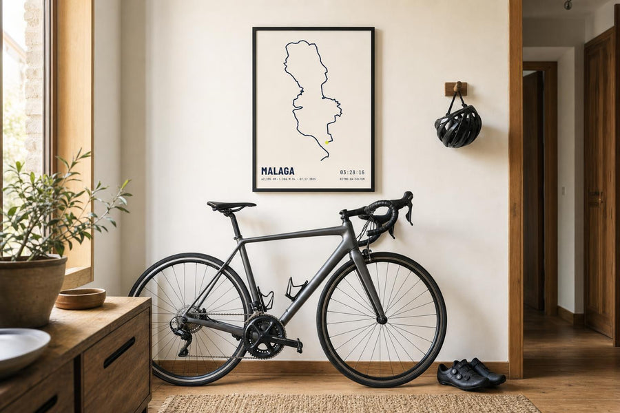 Bicicleta de carretera apoyada en la pared de un recibidor, bajo un cuadro con el trazado de una ruta.